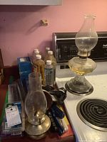 Glass oil lamps, oil containers, goggles and other accessories on stove top and counter, showing lamps in detail.