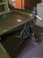 Side view of antique relief printing press showing cast iron base with crank and laminate topped work surface.