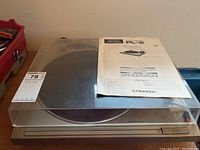 Full view of the turntable with dust cover and manual on top, showing front and top sides.