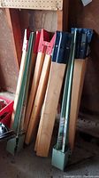Four wooden sawhorse legs with two red and two blue powder-coated steel top brackets leaning against a wall.