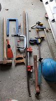 Overview of all items in the lot arranged on the ground including sledgehammer, clamps, pry bars, saw, and hard hat