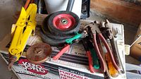 Yellow scissor car jack, two wheels with red rims, clamps, and other metal hand tools on top of a cardboard box.