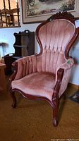 Front view of pink velveteen upholstered Victorian wing back chair showing carved wooden frame and floral engraving on top crest rail.