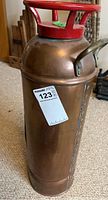 Side view of vintage copper fire extinguisher with red handle and MaxSold sticker.