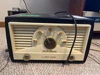 Front view of vintage Baby Champ radio showing dial, knobs, and attached power cord.