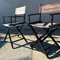 Two directors chairs outdoors on concrete, showing black and white canvas seats and backs with black wood frames and foldable design.