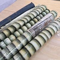 Six wallpaper rolls laid out on a table, five with bamboo pattern and one blue floral pattern.