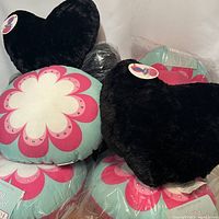 Photo showing black heart-shaped plush pillows and turquoise circle pillows with pink and white flower design, both brand new with tags.