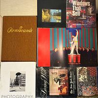 Top view of multiple coffee table books including 'Rembrandt', 'Store Windows That Sell', 'Photography' and 'The New York Times 20th Century Design' arranged in a square layout.