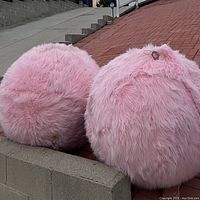 Two large pink furry balls made of Styrofoam and covered with pink fabric, resting on a low concrete wall.