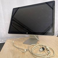 Front view of the Apple iMac external monitor on its aluminum stand with attached cables visible on the table.