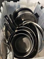 Overview of stacked pots and pans including lids inside a plastic bin