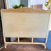 Front view of rattan and wicker headboard showing carved top edge and wicker panel body.