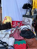 Various purses, totes, handbags, and backpacks stacked and displayed against a white backdrop, showing assortment and condition.