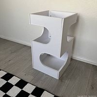 Front view of white geometric shaped shelf unit with curved cutouts and visible minor edge lifting.
