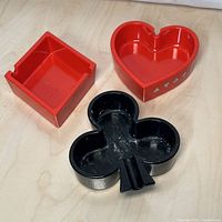 Set of three ashtrays shaped like playing card suits: heart (red), diamond (red), and club (black) placed on a wood surface, showing the front and top.