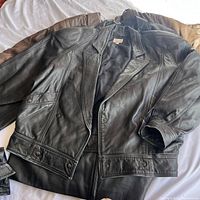 Black biker-style leather jacket spread flat showing front zip, snap collar and upper pockets