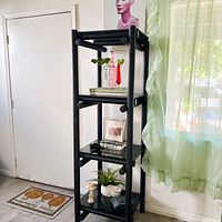 Full front view of the vintage black chrome metal shelf with four tinted smoke glass shelves, displayed with books and decorative items.
