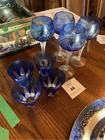 Two sets of cobalt blue glass cordial goblets featuring cut-to-clear floral and geometric patterns, displayed on wooden table.