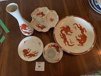 Wide view of the full set on wood table, showing detailed red dragon motifs on all porcelain pieces including the vase, plate, teacup set, and divided dish.