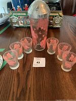 Full shot of cocktail shaker with six shot glasses arranged around it, all decorated with pink dancing elephant and stars.