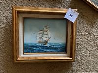 Framed oil painting showing a ship sailing on the ocean with birds flying in the sky.