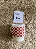 Front view of vintage Fire King milk glass mug with red checkerboard design.