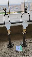 Pair of vintage metal desk lamps standing side by side on carpeted floor near window, showing height and base size.