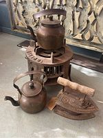 Photo showing antique cast iron stove with a vintage kettle on top, smaller kettle and antique iron placed beside