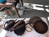 Overview of all antique Indian chappatti rollers and plates on white table, showing cast iron plates, wooden plates, and wooden rollers.
