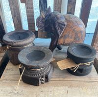Three black wooden artisan candle holders with a rustic finish placed on a wooden surface beside a hand-carved wooden elephant sculpture, showing the original shape from antique seed spreaders.