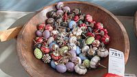 Photo showing a large wooden bowl filled with assorted colorful ceramic door and cabinet knobs, various designs and colors visible, metal screws attached.