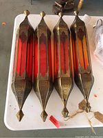 Four artisan punched tin hanging candle holders laid side by side showing red translucent side panels and brass finish with detailed perforations.
