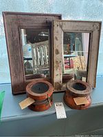 Two rustic artisan mirrors with wooden distressed frames and two round wooden candle holders on a counter.