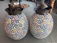 Overall front view of two oval-shaped artisan mosaic glass lamp housings with metal tops, showing colorful floral mosaic patterns.