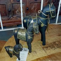 Three wooden horses with dark polish and brass decorations on wooden table, showing scale and details
