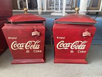 Two red vintage-style Coca-Cola coolers side by side, showing front logos, lids, and handles.