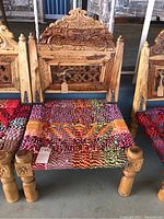 Front view of the Indian artisan folding low chair showing the carved wooden backrest and the colorful woven seat.