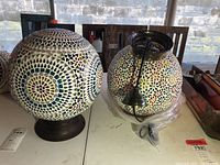Two round mosaic glass lamp housings on dark bases, one with electrical components, one without, shown from front and side angle.