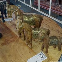 Photo of three hand carved wood horses with hammered brass details on their saddles and heads, arranged on wooden surface.