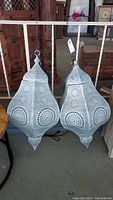 Two punched tin hanging pendant lights with intricate circular patterns, silver paint with some scratches and one dent shown hanging side by side.