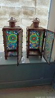 Pair of antique metal housing mosaic glass candle lanterns with open doors, showing intricate circular mosaic designs and patina on metal.