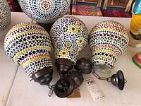 Three bulb-shaped mosaic colored glass lamp housings with metal caps and hanging hardware. Arranged close together on a flat surface.