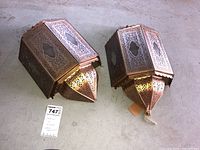 Two Indian tin filigree lamp housings side by side on floor showing shape and perforated designs