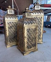 Three gold-tone enameled tin Moroccan-style candle lanterns with filigree panels and domed tops grouped together