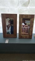 Two similar rustic reclaimed wood framed mirrors side by side on a display surface against a white wall.