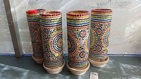 Four cylindrical mosaic lamp housings shown from side angle, displaying colorful geometric and floral handmade glass mosaics in vibrant colors.