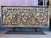 Front view of the rectangular hand carved wood art mounted on a metal stand, showing decorative patterns and distressed finish.