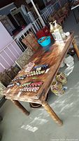 Photo of rectangular reclaimed wood dining table with metal hook accents along sides placed on concrete floor with assorted decorative items on and under the table.