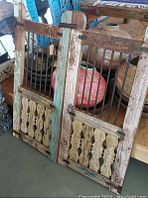 Two reclaimed wood 2-piece gate doors leaning against furniture, showing metal bars inset and decorative wood slats with rustic painted finishes and visible wear.